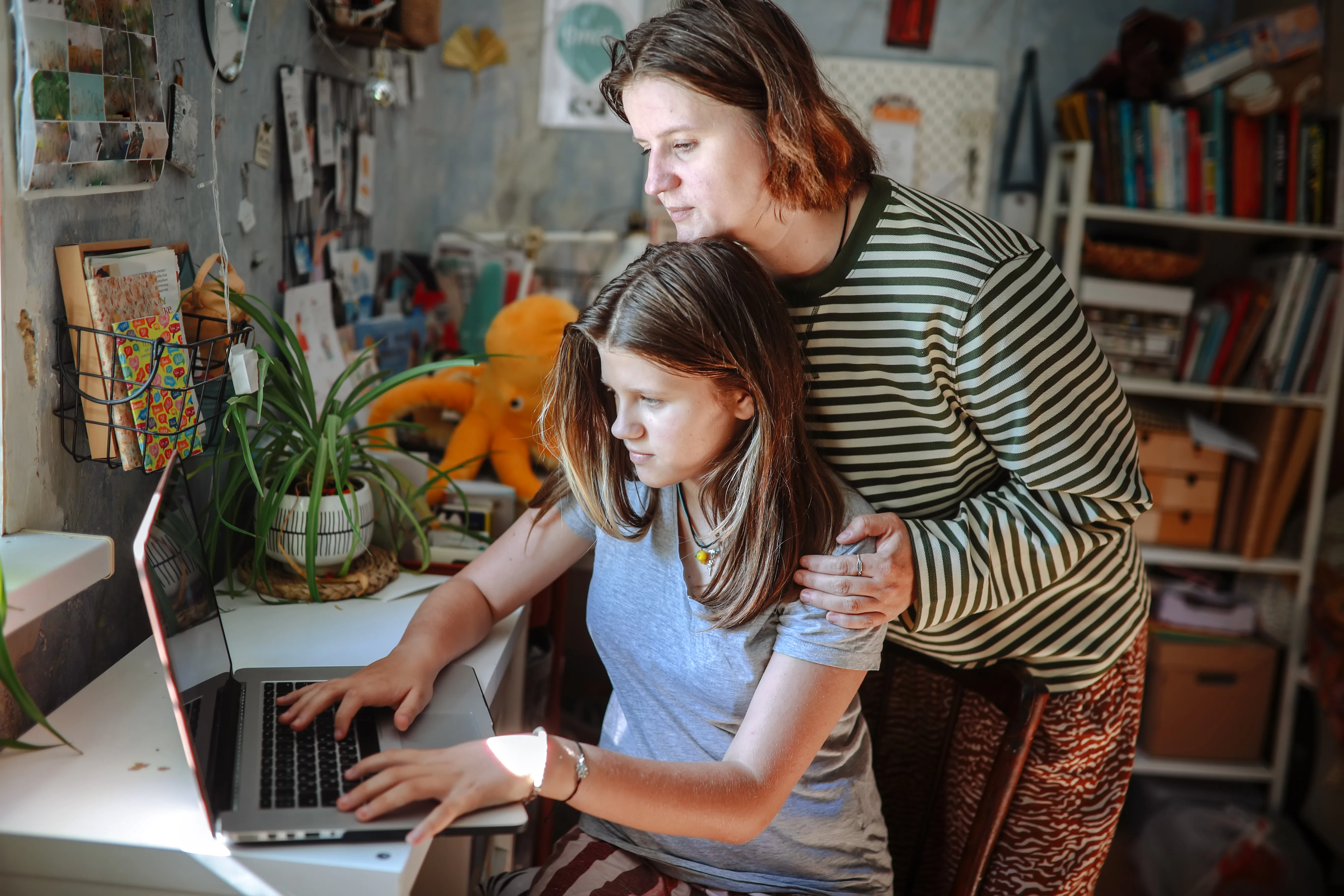 Plus-size middle-aged mom and teenage daughter working together on a laptop at home, academic suppor...