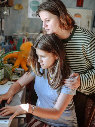 Plus-size middle-aged mom and teenage daughter working together on a laptop at home, academic suppor...