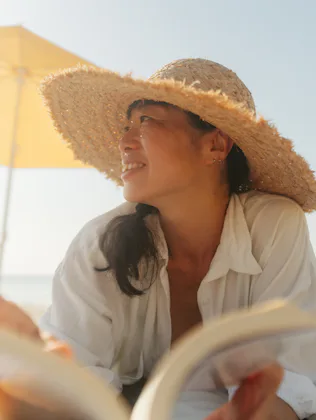 Photo of an Asian woman enjoying a day at the beach while reading a book by the sea