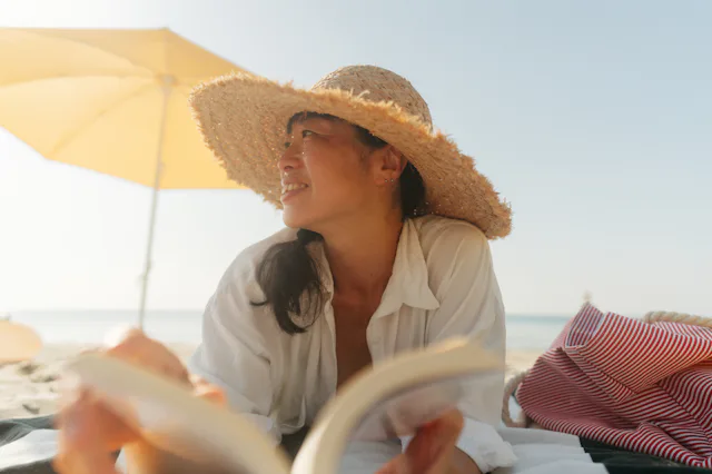 Photo of an Asian woman enjoying a day at the beach while reading a book by the sea