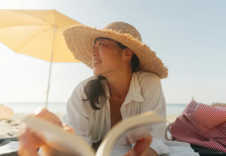 Photo of an Asian woman enjoying a day at the beach while reading a book by the sea