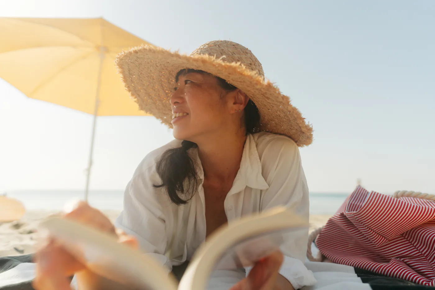 Photo of an Asian woman enjoying a day at the beach while reading a book by the sea