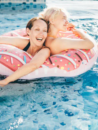 Family enjoying the hotel pool during summer vacation. Mother and daughter enjoyment in swimming poo...
