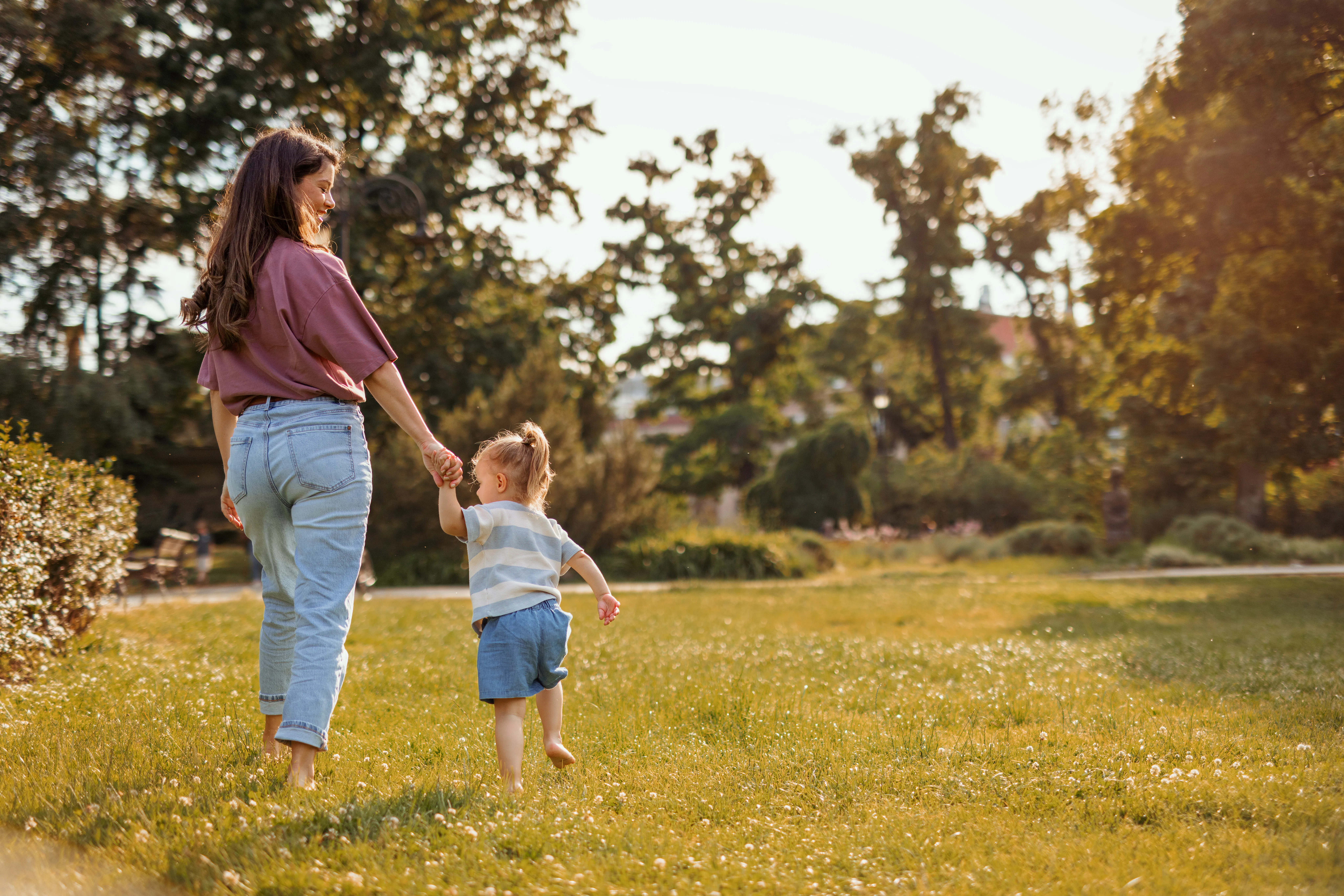 A mom and toddler walking through grass. 