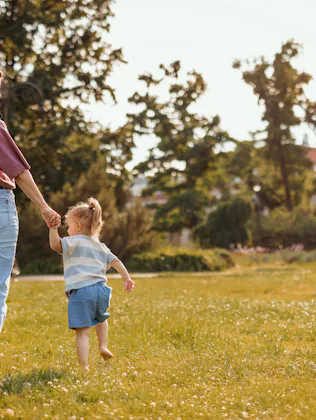A mom and toddler walking through grass.
