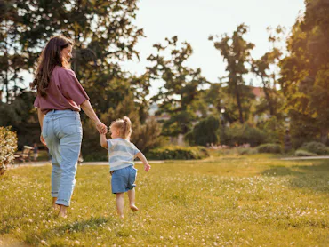 A mom and toddler walking through grass.