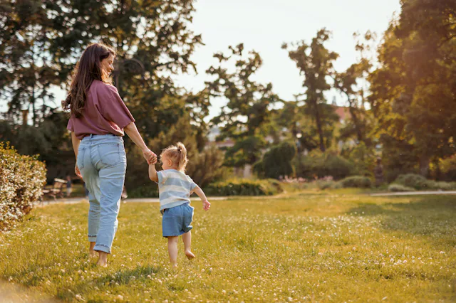 A mom and toddler walking through grass.