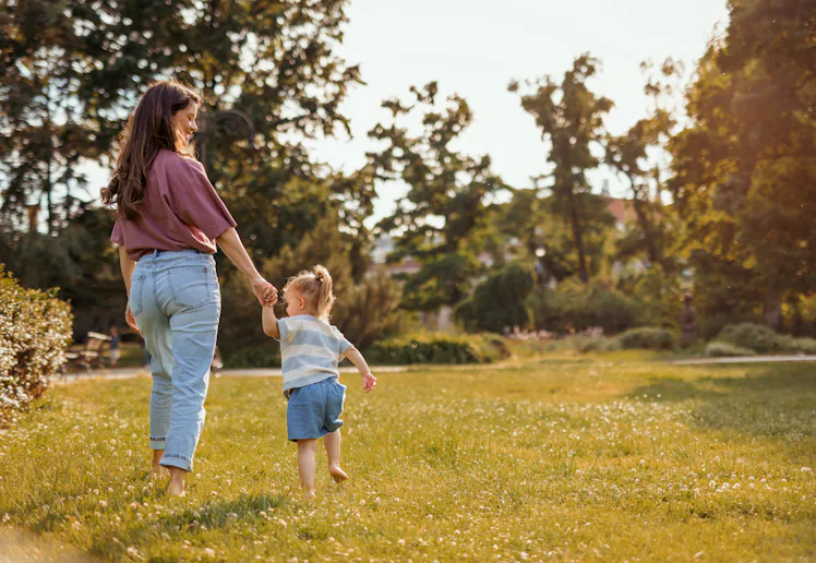 A mom and toddler walking through grass.