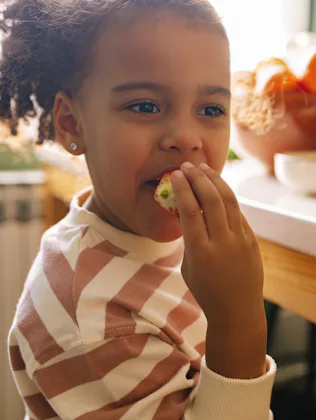 Young Afro-American girl eating a strawberry in the kitchen.