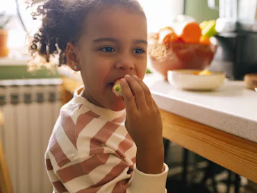 Young Afro-American girl eating a strawberry in the kitchen.