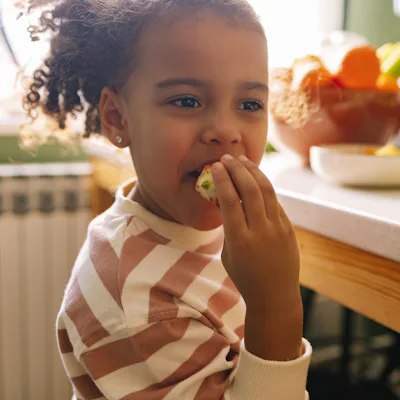 Young Afro-American girl eating a strawberry in the kitchen.