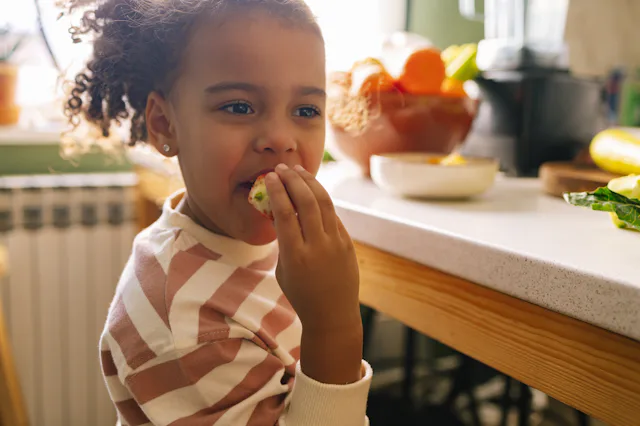 Young Afro-American girl eating a strawberry in the kitchen.