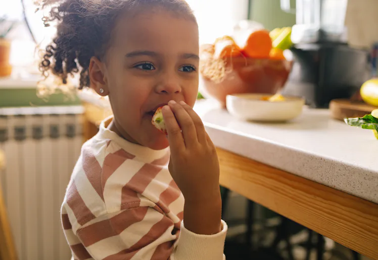 Young Afro-American girl eating a strawberry in the kitchen.
