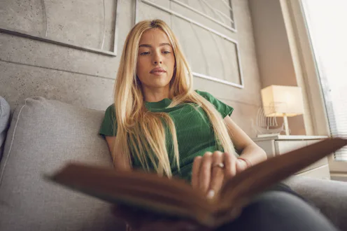 Women wellness. Low angle view of beautiful Gen Z Asian woman reading book in calm cozy home atmosph...