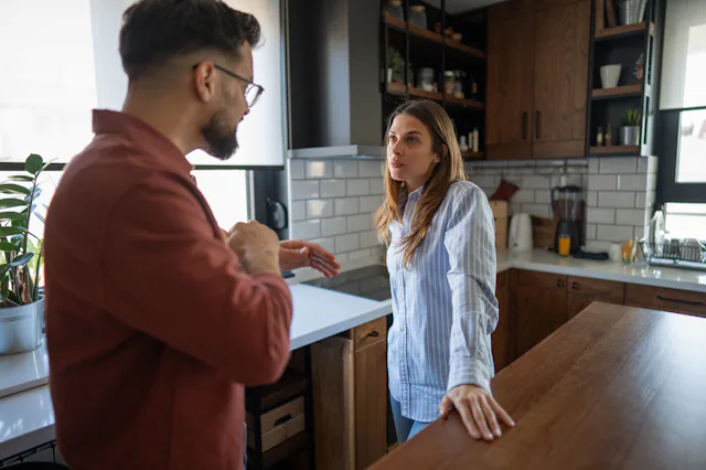 Couple having a difficult conversation in their kitchen, experiencing relationship problems, conflic...