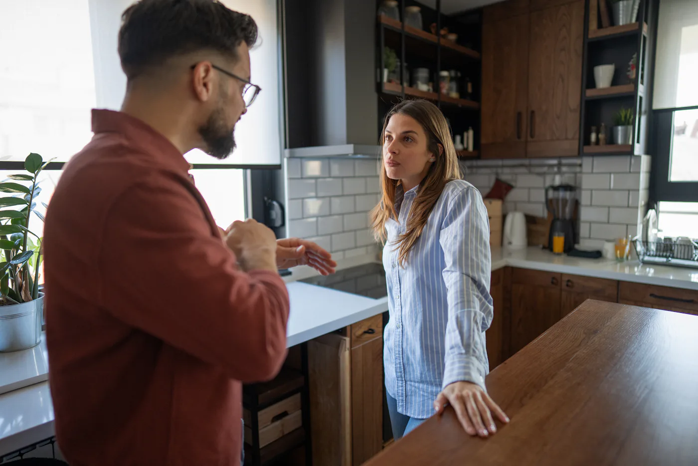 Couple having a difficult conversation in their kitchen, experiencing relationship problems, conflict, and misunderstanding while standing in a modern home interior