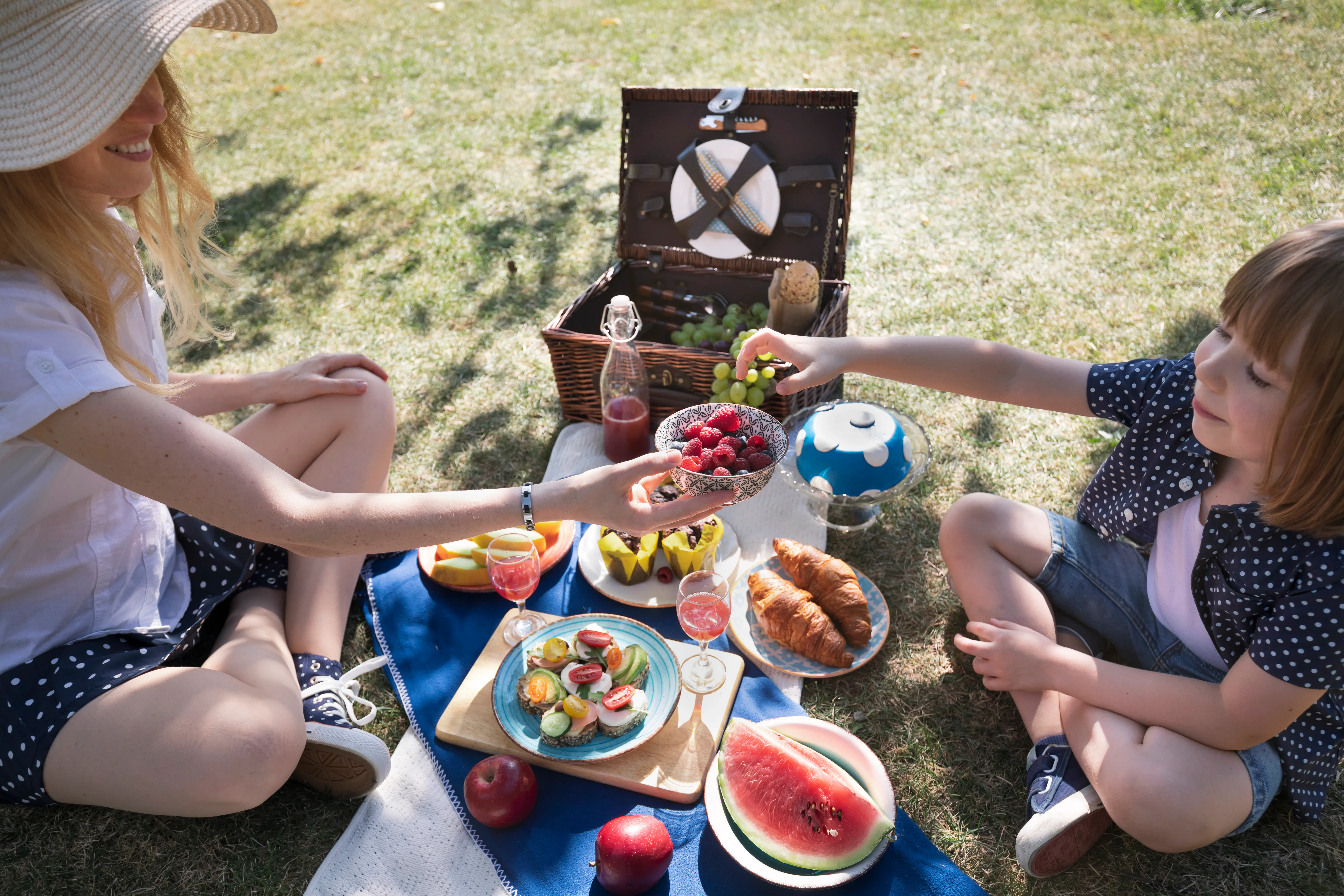 Mother and child share a bowl of raspberries and blueberries surrounded by drinks, croissants and fr...