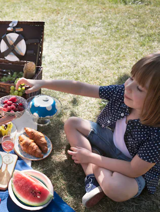 Mother and child share a bowl of raspberries and blueberries surrounded by drinks, croissants and fr...