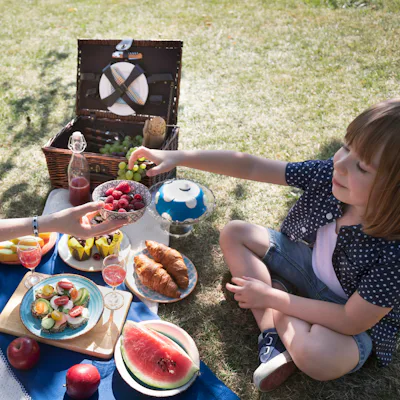 Mother and child share a bowl of raspberries and blueberries surrounded by drinks, croissants and fruit. Food photography, summer lifestyle, family leisure and healthy snacking themes.