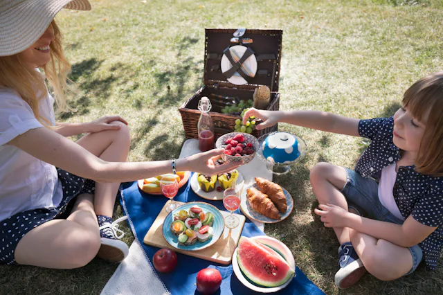 Mother and child share a bowl of raspberries and blueberries surrounded by drinks, croissants and fr...