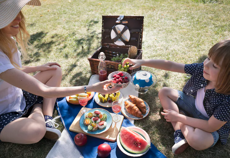 Mother and child share a bowl of raspberries and blueberries surrounded by drinks, croissants and fr...