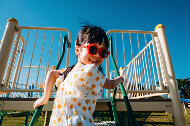 Joyful little Asian girl having fun playing at jungle gym in an outdoor playground on a lovely sunny...