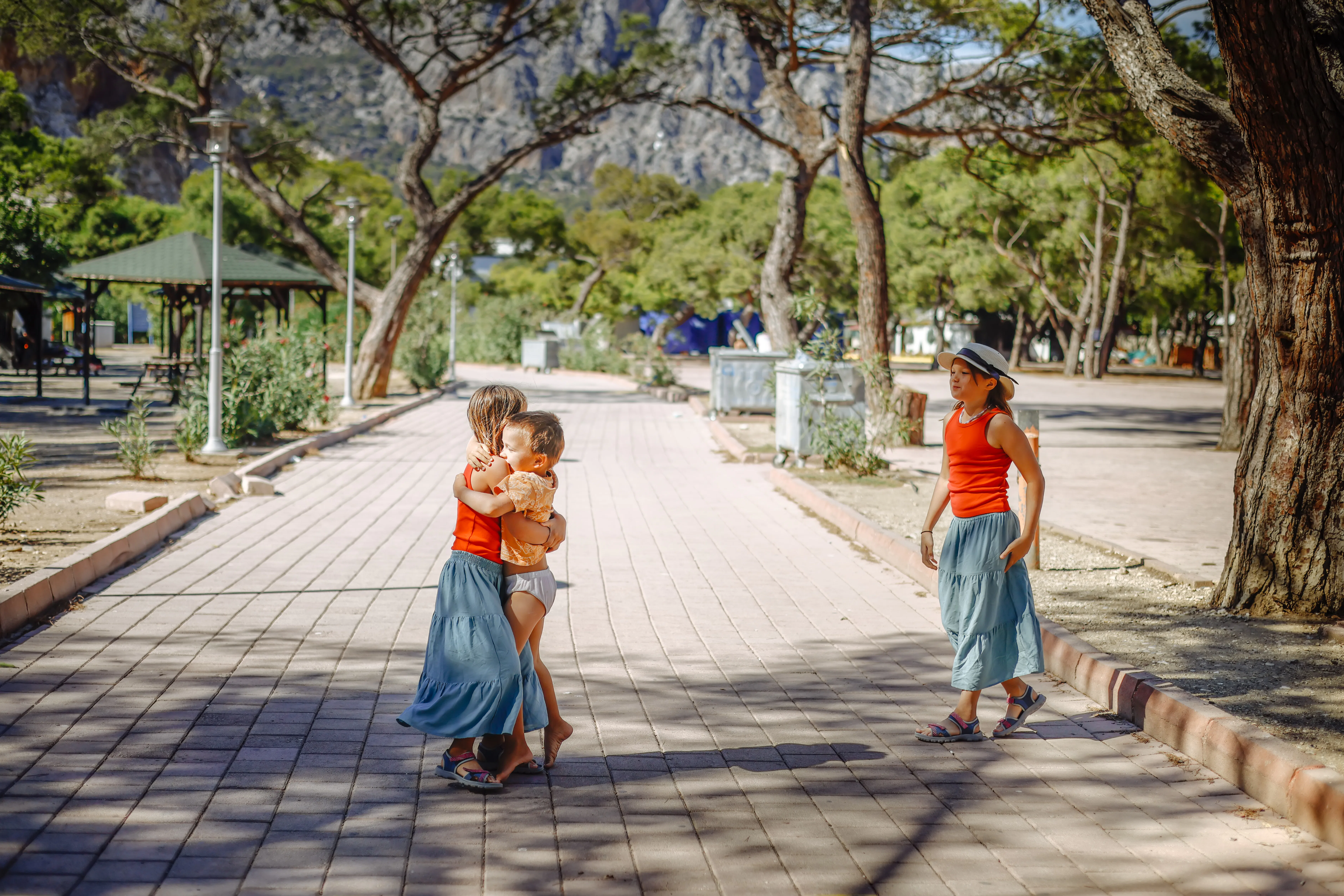 Three sibling children together on a path in a sunny pine park, moments of a walk with children.