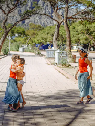 Three sibling children together on a path in a sunny pine park, moments of a walk with children.