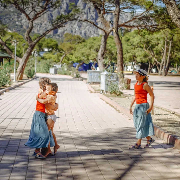 Three sibling children together on a path in a sunny pine park, moments of a walk with children.
