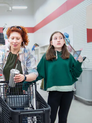 Middle-aged woman with curly red hair shops with her young daughter at a supermarket checkout. The m...