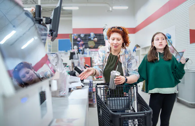 Middle-aged woman with curly red hair shops with her young daughter at a supermarket checkout. The m...