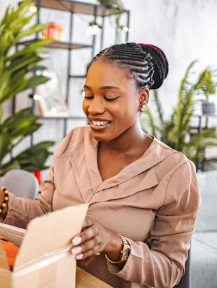 Young adult woman opening a delivered cardboard box with a cheerful expression