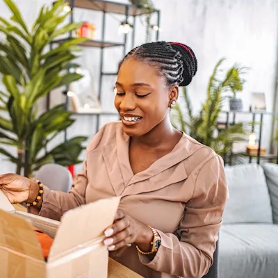 Young adult woman opening a delivered cardboard box with a cheerful expression