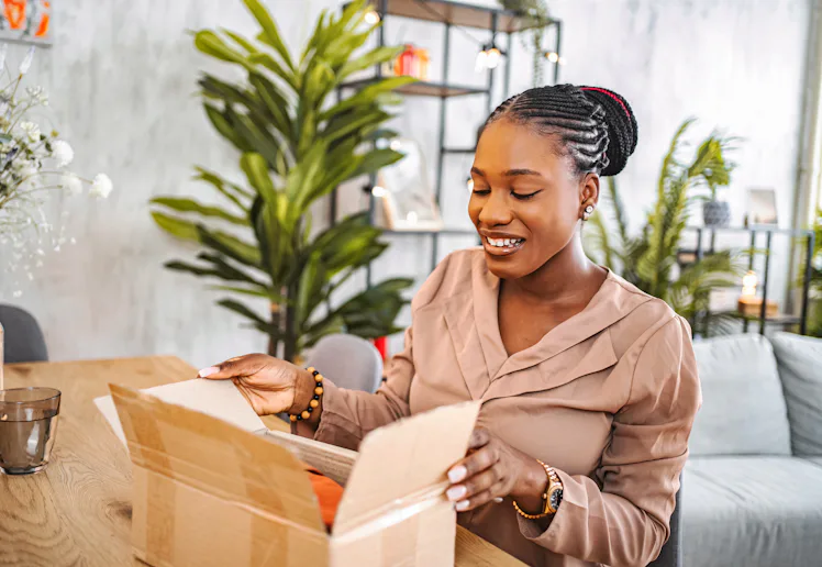 Young adult woman opening a delivered cardboard box with a cheerful expression