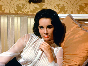 Elizabeth Taylor (1932-2011), British actress, wearing a sheer white blouse reclining against a cush...