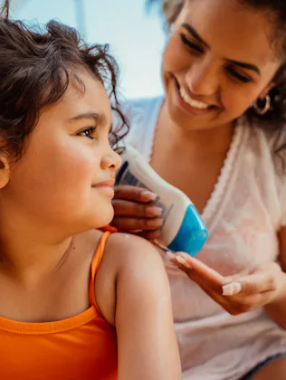 Mother putting sunscreen on her daughter before going into the pool
