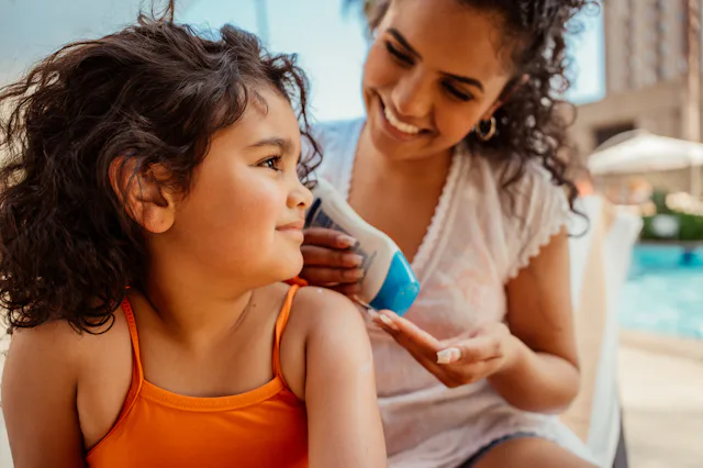 Mother putting sunscreen on her daughter before going into the pool