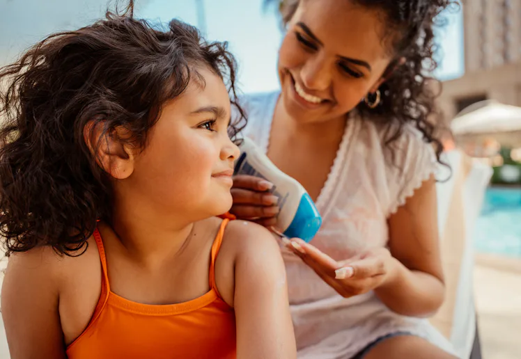 Mother putting sunscreen on her daughter before going into the pool