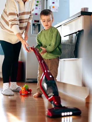 Young woman teaching her little son to use a vacuum cleaner