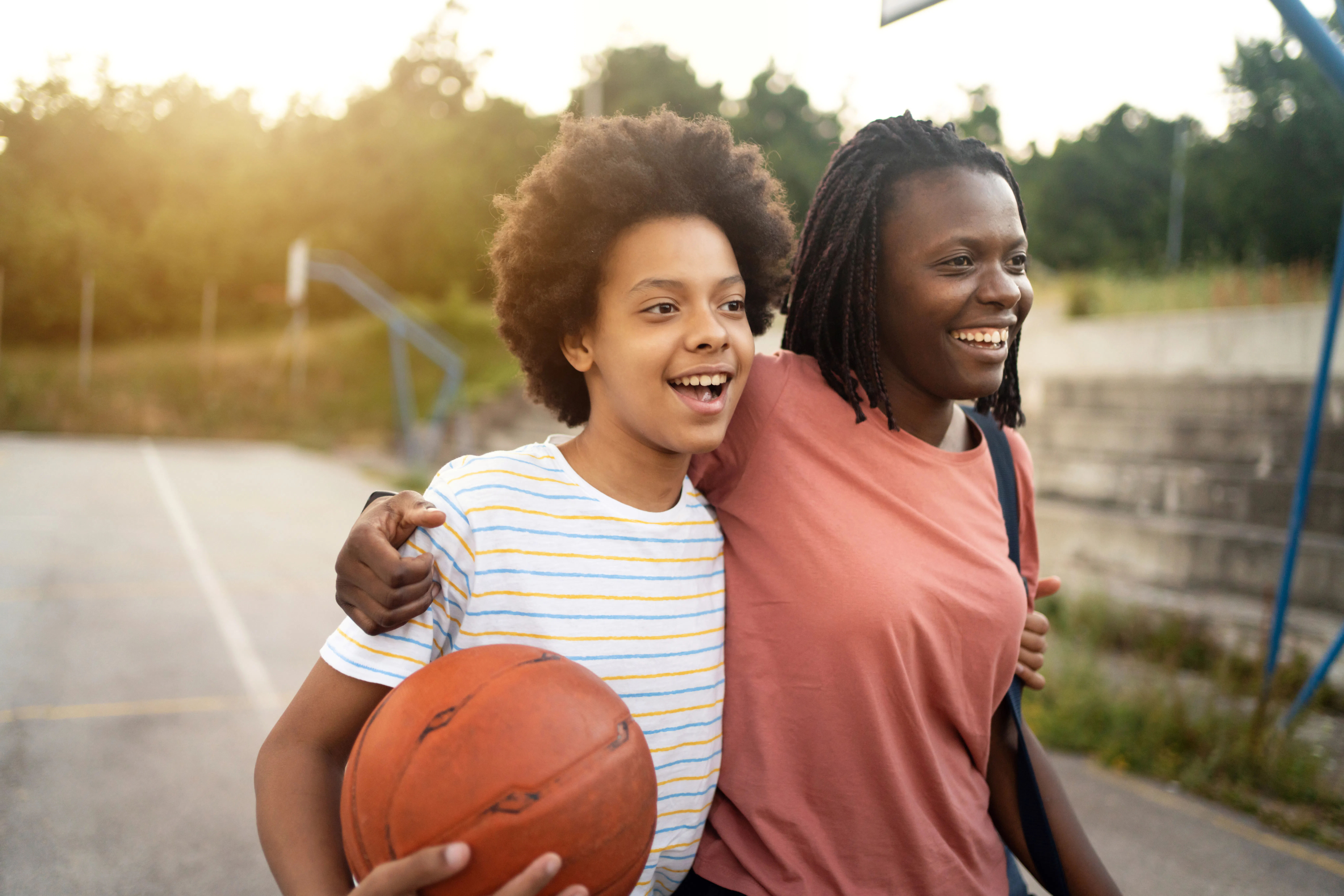 Embraced mother and daughter of Black ethnicity, going home after they finished with outdoor basketb...