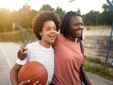 Embraced mother and daughter of Black ethnicity, going home after they finished with outdoor basketb...