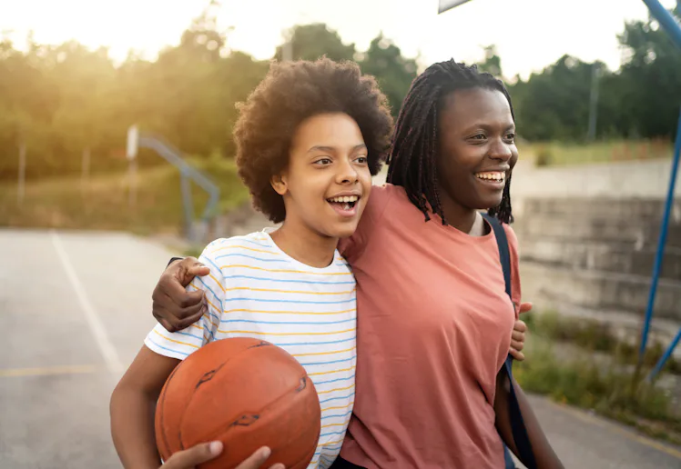 Embraced mother and daughter of Black ethnicity, going home after they finished with outdoor basketb...