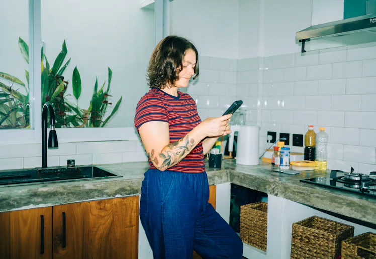 Woman smiling using smartphone in kitchen