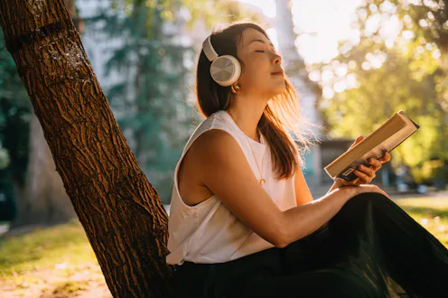 Young Asian woman enjoying a relaxing moment, reading a book in the park. Wellbeing and mental healt...