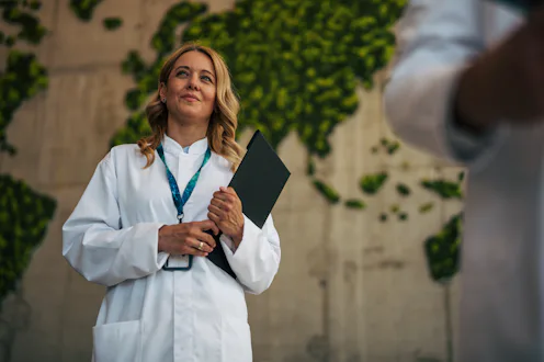Female scientist holding a folder and looking up, standing in a modern office with a green living wo...