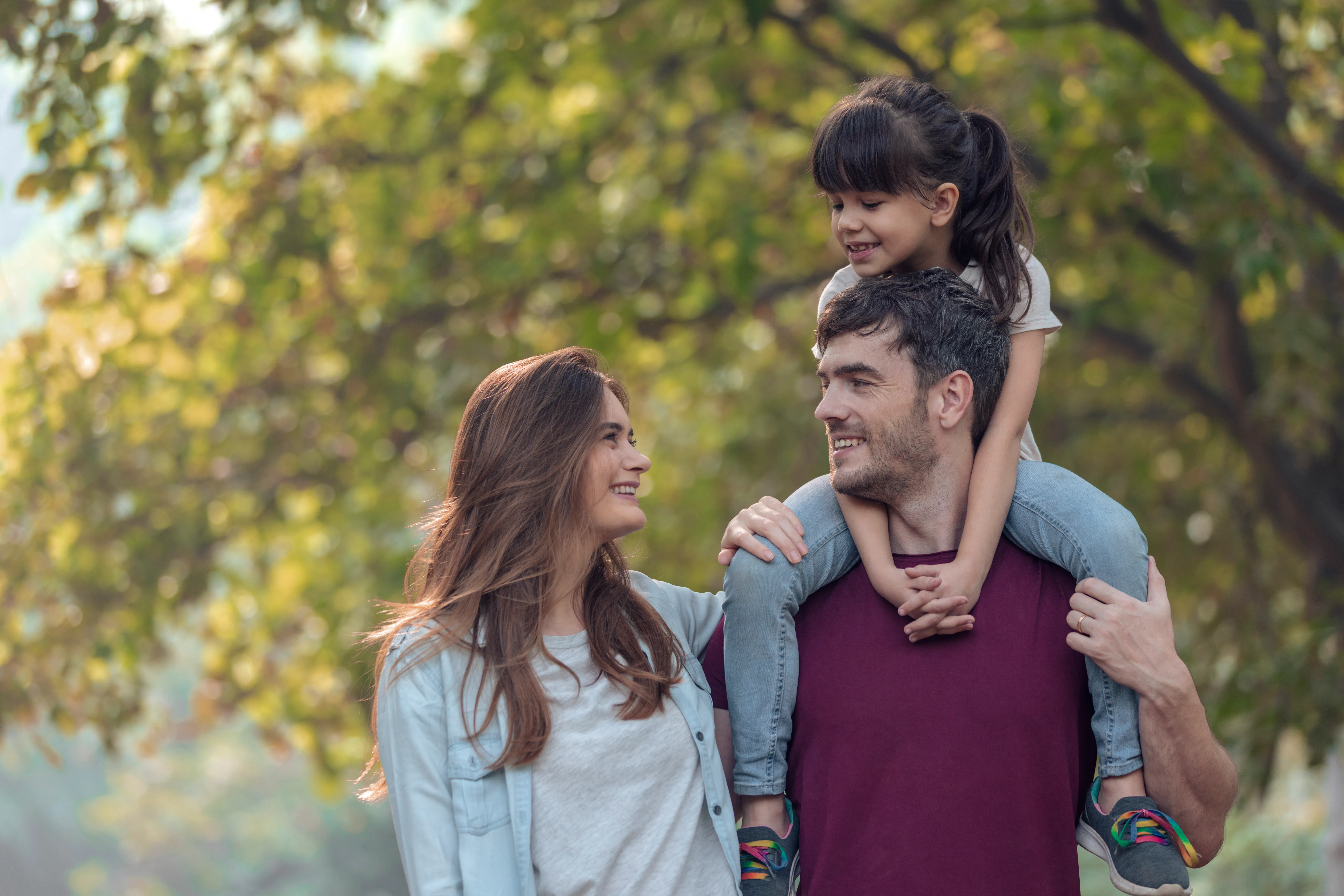 Smiling parents with daughter spending leisure time in public park.