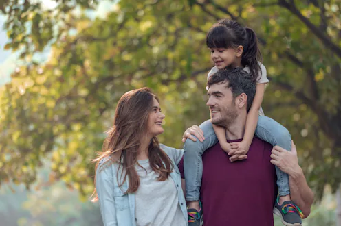 Smiling parents with daughter spending leisure time in public park.