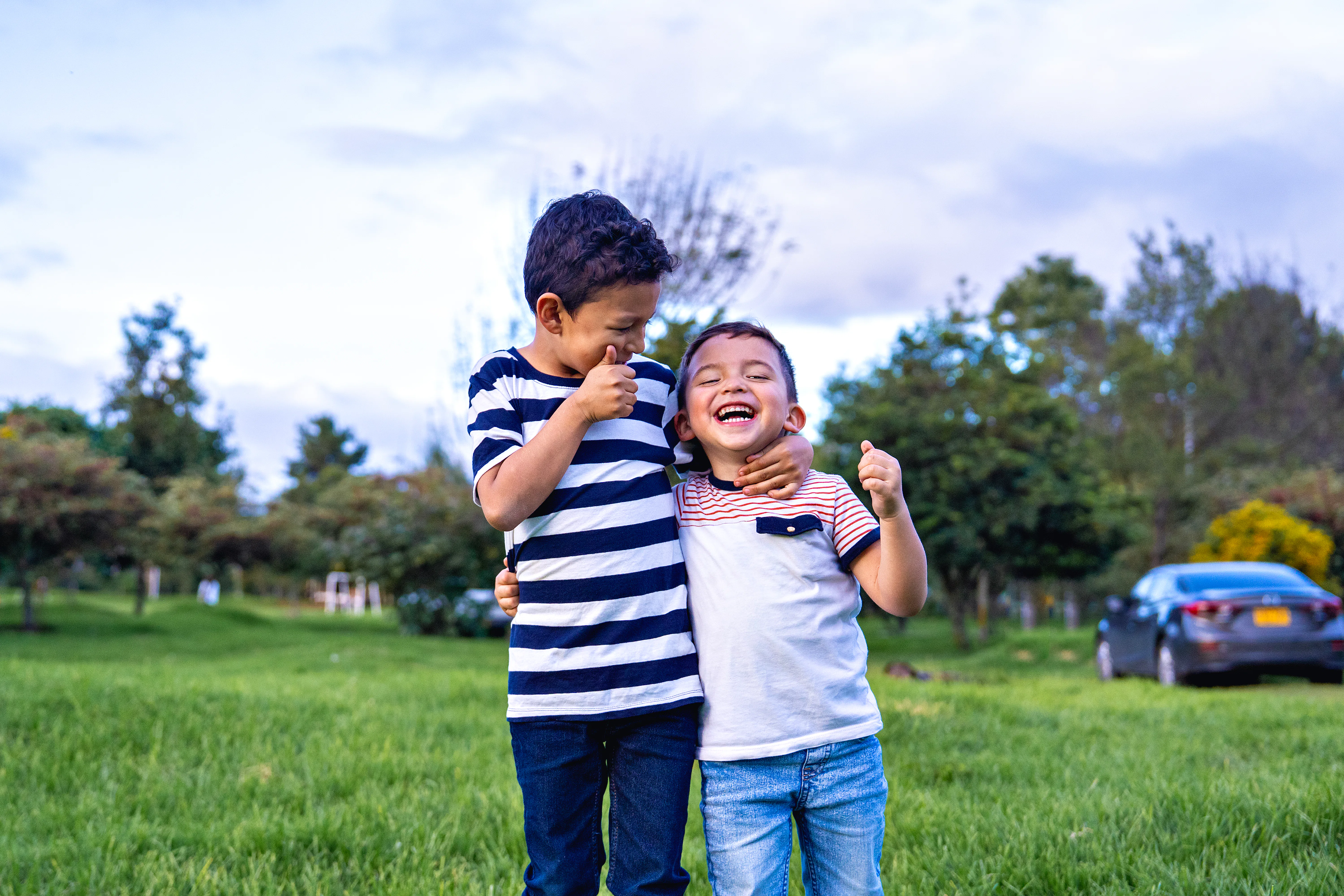 Two happy boys laughing and having fun in a green park, one waving his hand up in the air while the ...