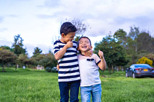 Two happy boys laughing and having fun in a green park, one waving his hand up in the air while the ...
