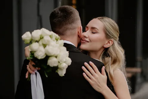 Joyful bride in flowing white gown and groom in tailored suit share an intimate moment, standing clo...